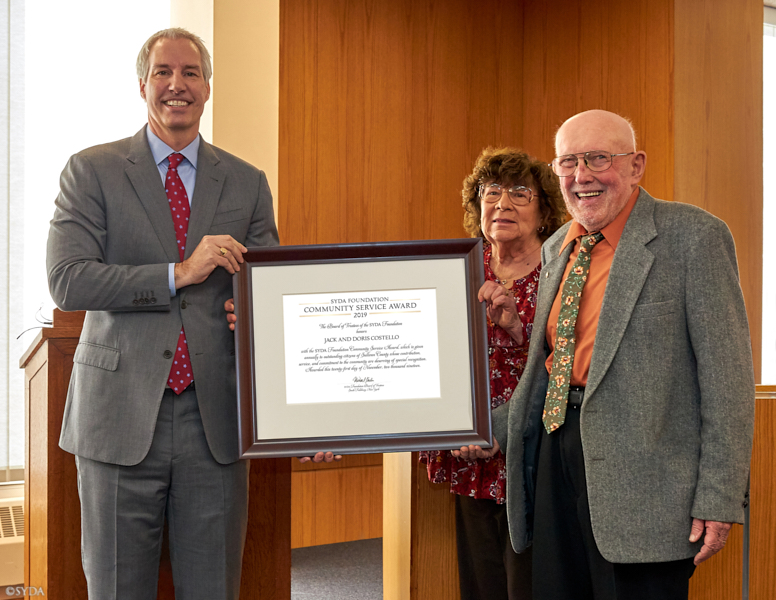 SYDA Foundation Representative presents a certificate of merit to Jack and Doris Costello